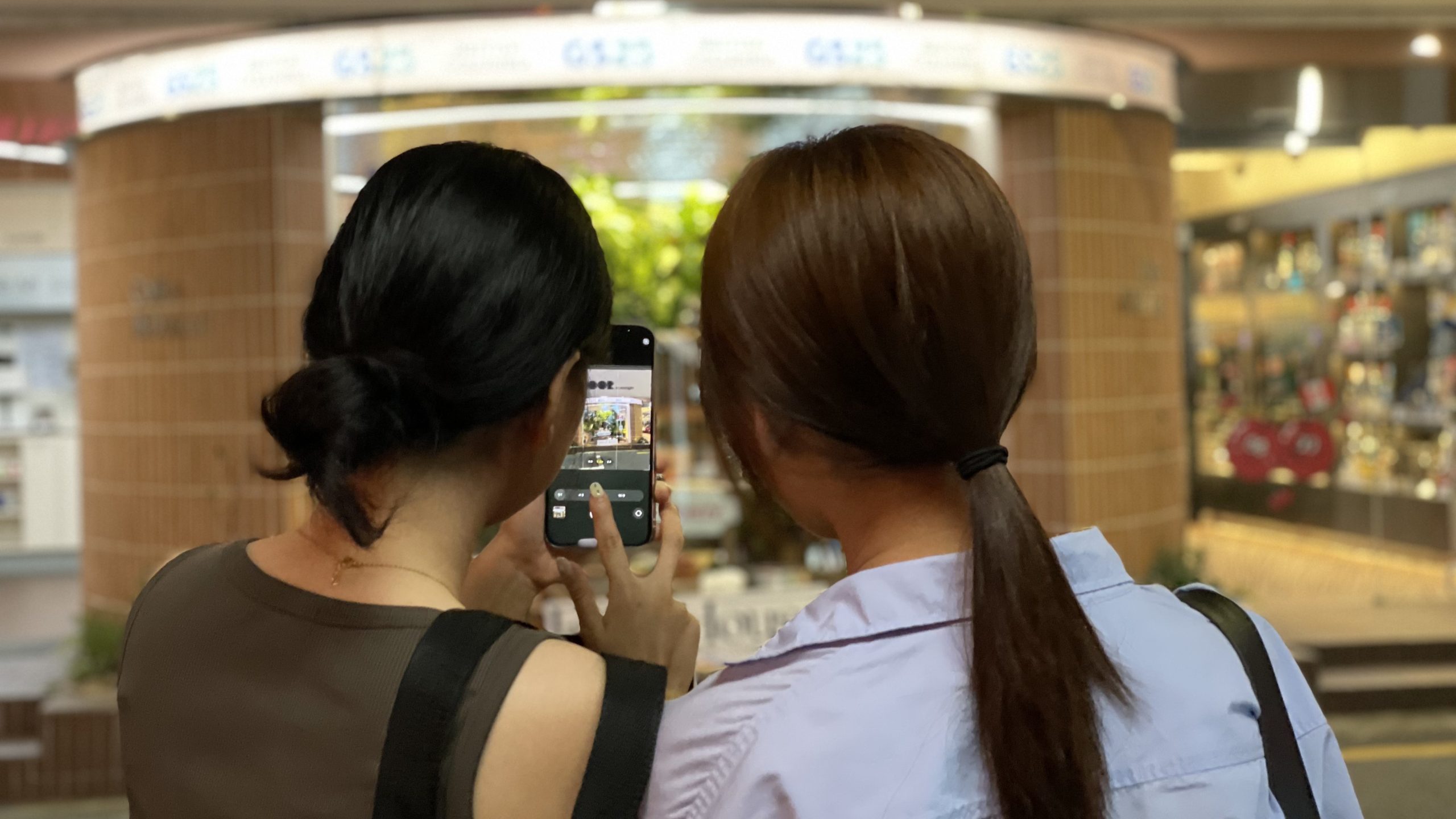 Two visitors with backs to camera using phone to post on social media.